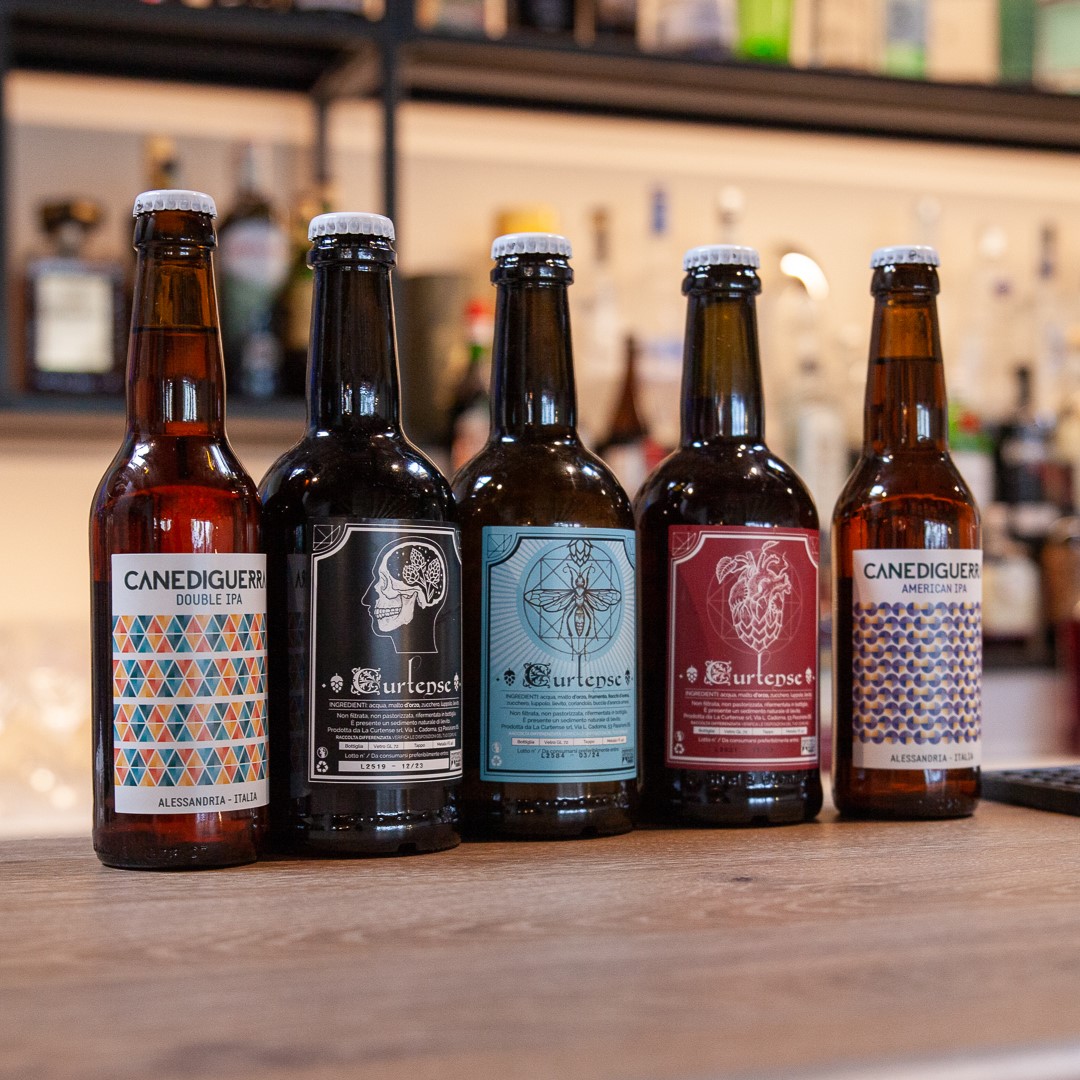 5 bottiglie particolari di birra una di fianco all'altra con sfondo vetreria del bar