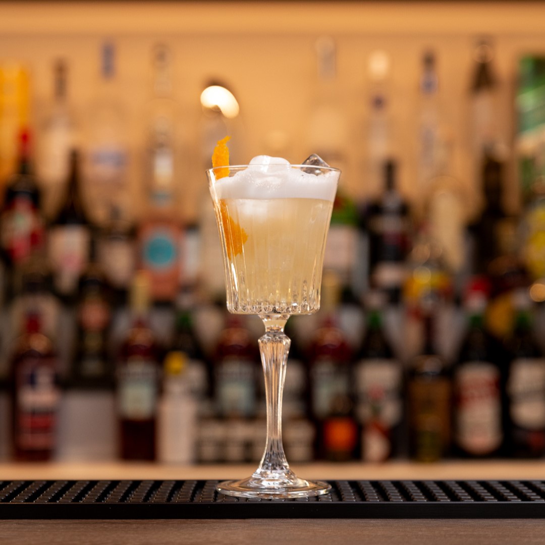 bicchiere da drink sopra al bancono con sfondo bottiglie su vetreria