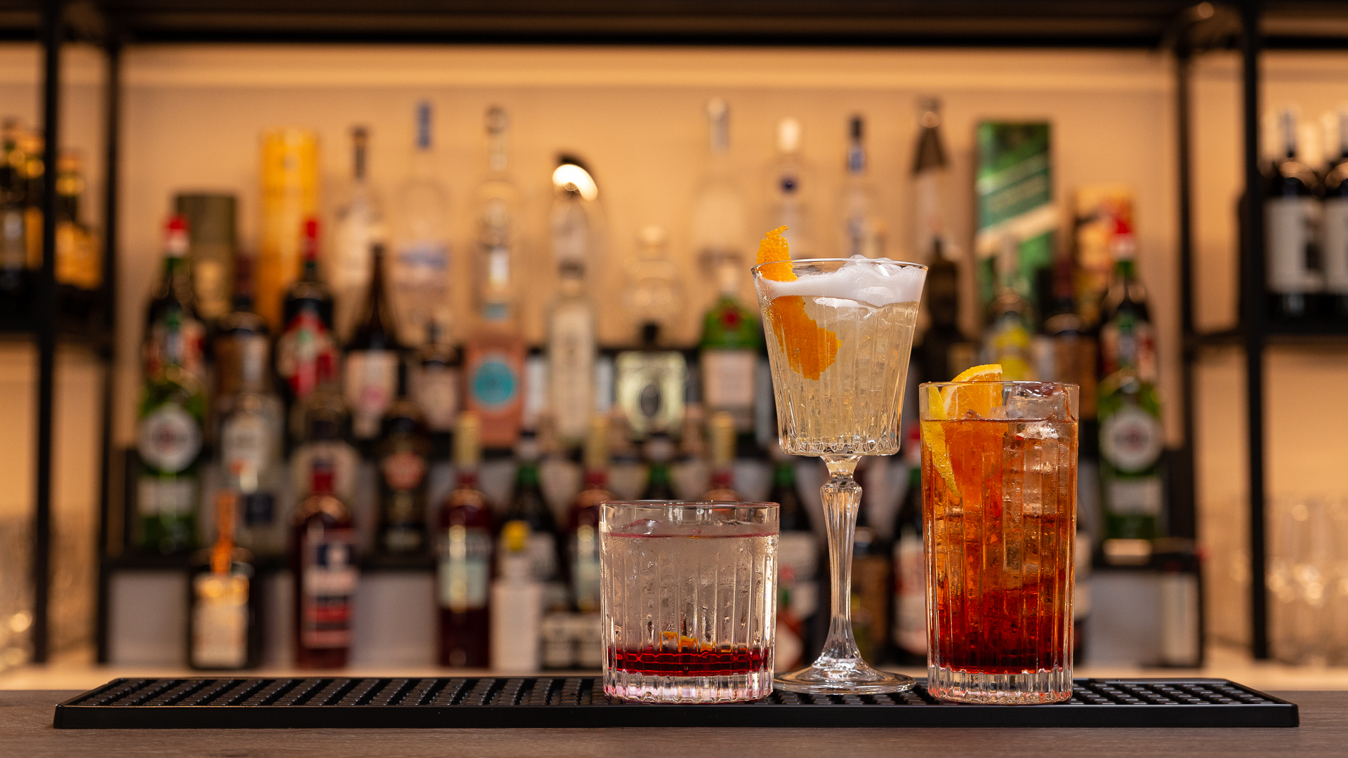 3 cocktail in bicchieri diversi con sfondo vetreria